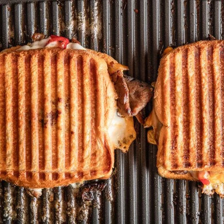 Two grilled sandwiches on a grill with visible grill marks.